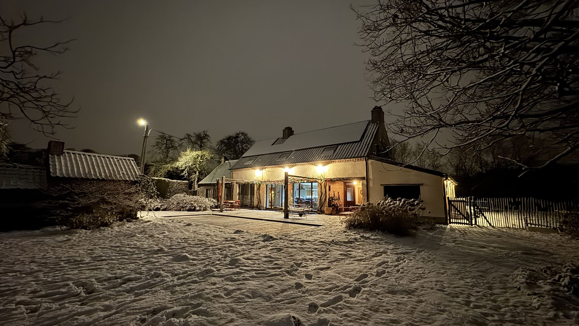 Ons huis 's avonds in de sneeuw, met de lichten aan onder de pergola